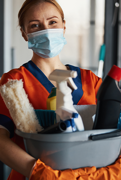 Cleaner in a face mask showing her cleaning products